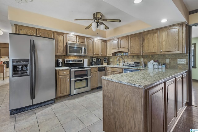 kitchen featuring light tile patterned flooring, stainless steel appliances, a peninsula, a sink, and backsplash