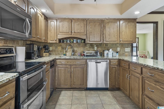 kitchen with tasteful backsplash, appliances with stainless steel finishes, brown cabinetry, and light stone countertops