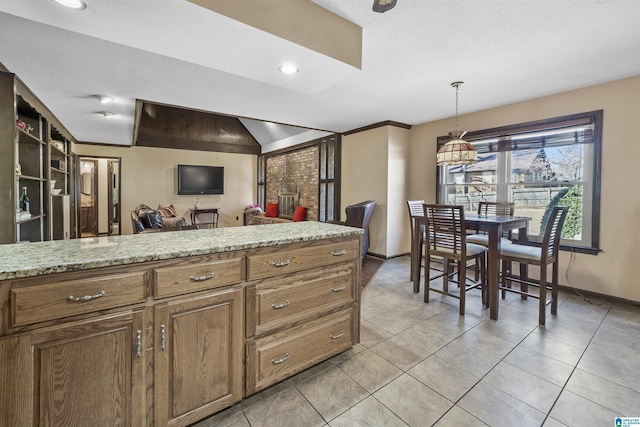 kitchen featuring light stone counters, hanging light fixtures, brown cabinetry, light tile patterned flooring, and baseboards