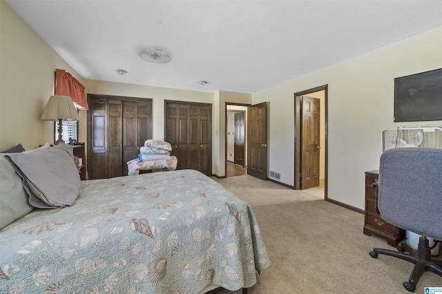 bedroom featuring multiple closets, visible vents, light carpet, and baseboards