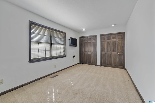 unfurnished bedroom featuring light colored carpet, visible vents, baseboards, and two closets