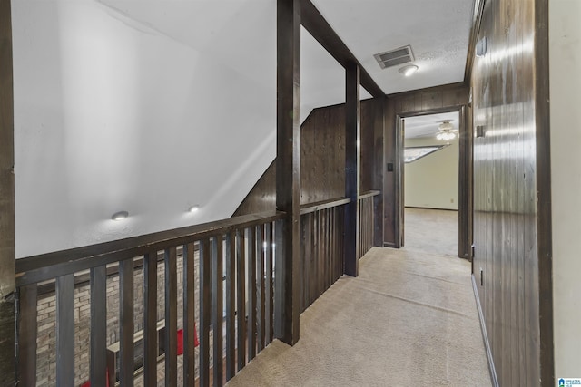 corridor with wood walls, visible vents, and light colored carpet