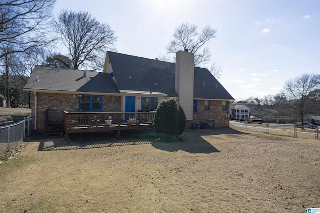 rear view of property featuring a chimney, brick siding, fence, and a deck