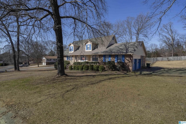 new england style home with an attached garage, brick siding, a front yard, and fence