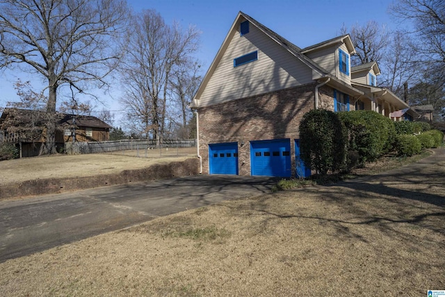 view of home's exterior with aphalt driveway, brick siding, fence, and an attached garage