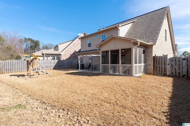 rear view of house featuring a sunroom, a fenced backyard, a patio area, a playground, and brick siding