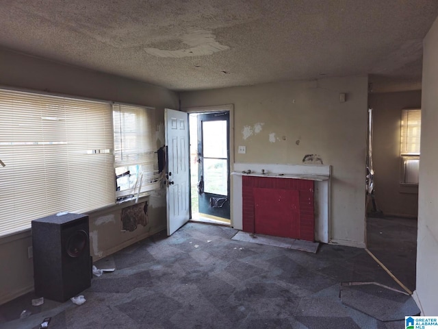 interior space featuring a textured ceiling, dark colored carpet, and a wood stove