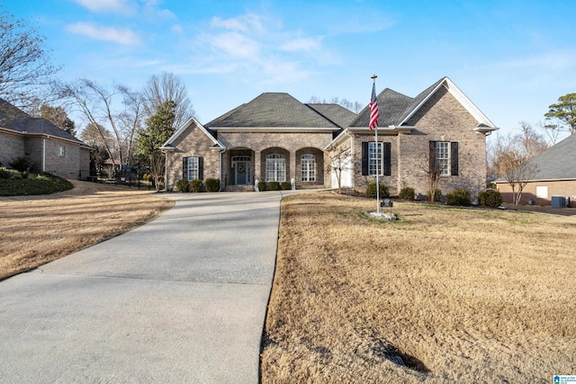 french country inspired facade featuring a front lawn, brick siding, and central air condition unit