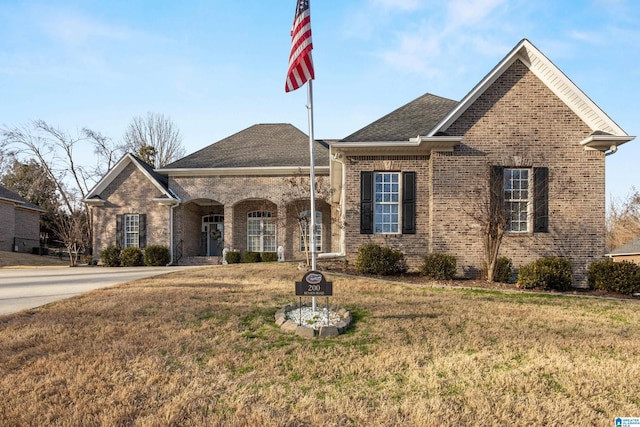 view of front of house with roof with shingles, a front lawn, and brick siding