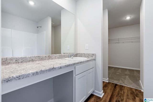 full bathroom with a walk in closet, recessed lighting, vanity, wood finished floors, and baseboards