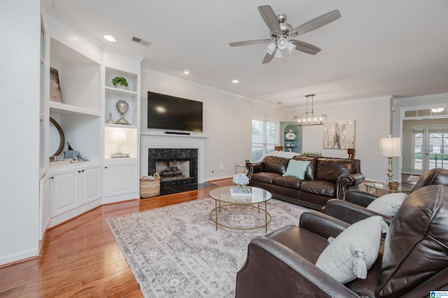 living area with built in features, crown molding, a high end fireplace, light wood-type flooring, and baseboards