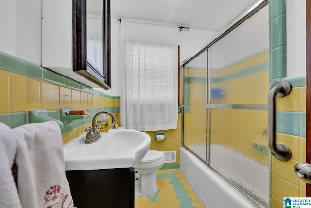 full bathroom featuring visible vents, toilet, shower / bath combination with glass door, vanity, and tile walls