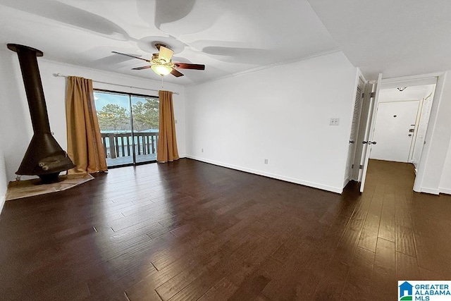 spare room featuring dark wood-style flooring, baseboards, ceiling fan, and a wood stove