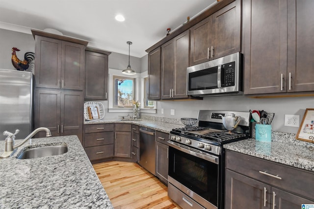 kitchen featuring stainless steel appliances, a sink, decorative light fixtures, and light stone countertops