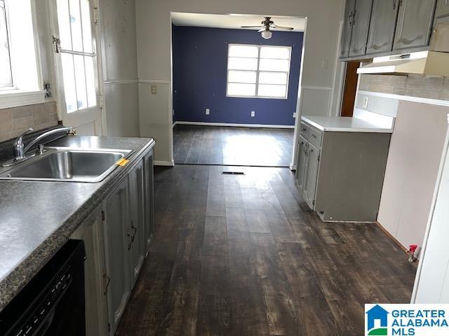 kitchen with under cabinet range hood, dark wood-style flooring, a sink, black dishwasher, and decorative backsplash