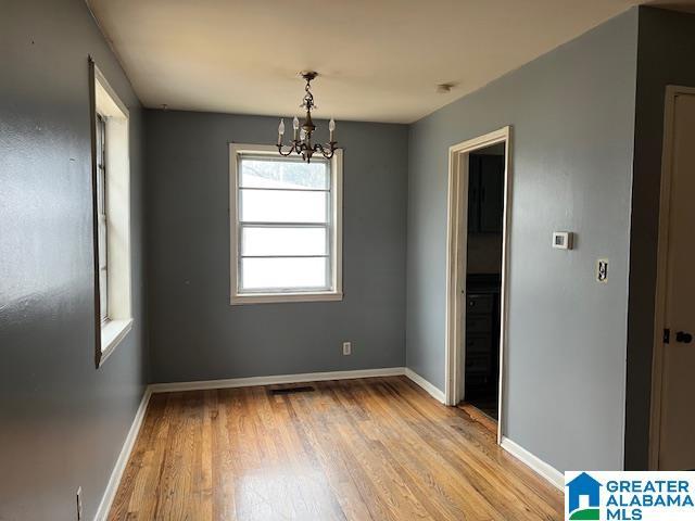 unfurnished dining area with light wood finished floors, an inviting chandelier, visible vents, and baseboards