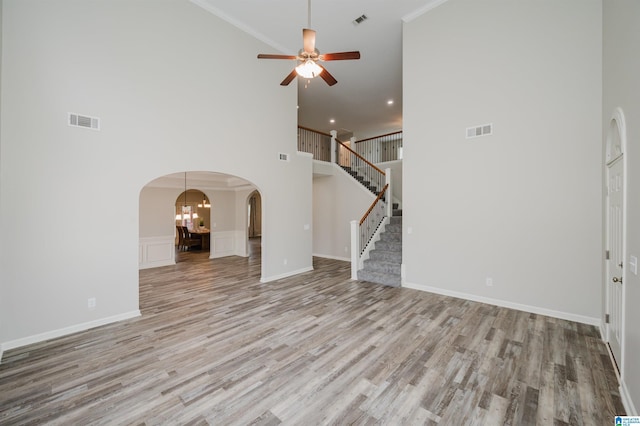 unfurnished living room featuring stairway, visible vents, arched walkways, and wood finished floors