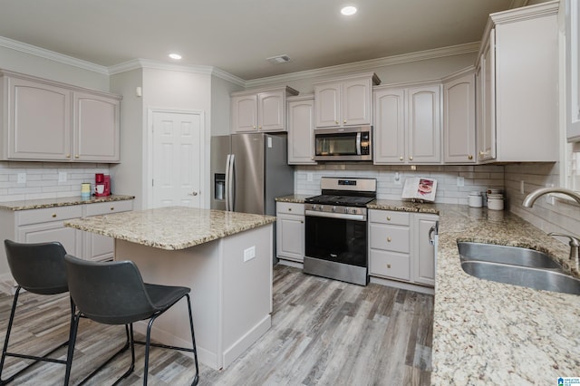 kitchen with stainless steel appliances, light wood-style floors, ornamental molding, a sink, and a kitchen breakfast bar