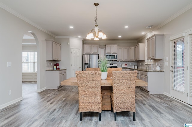 dining room with arched walkways, baseboards, crown molding, and light wood finished floors