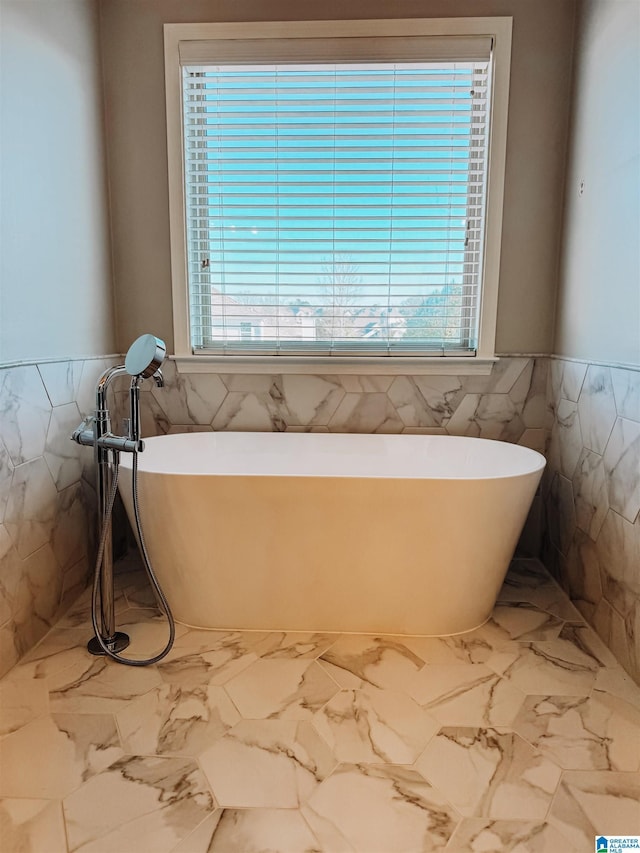 bathroom featuring marble finish floor, tile walls, and a wealth of natural light