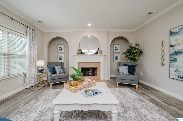 living area with ornamental molding, a tile fireplace, visible vents, and wood finished floors