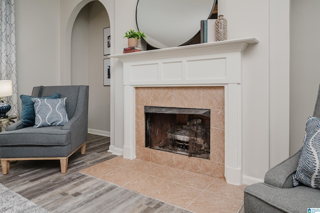 sitting room with arched walkways, a tiled fireplace, light wood-style flooring, and baseboards