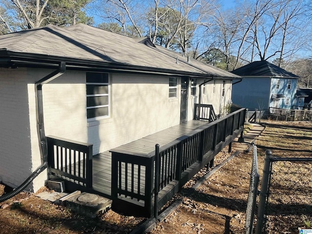 view of side of property with brick siding, fence, a wooden deck, and roof with shingles