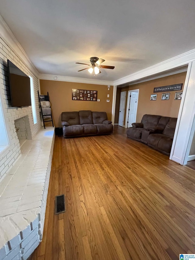 unfurnished living room with light wood-style flooring, a ceiling fan, visible vents, a brick fireplace, and crown molding