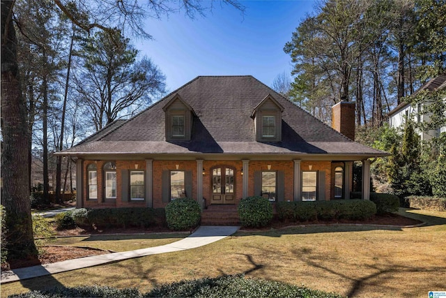 view of front facade featuring a shingled roof, covered porch, a chimney, and a front lawn