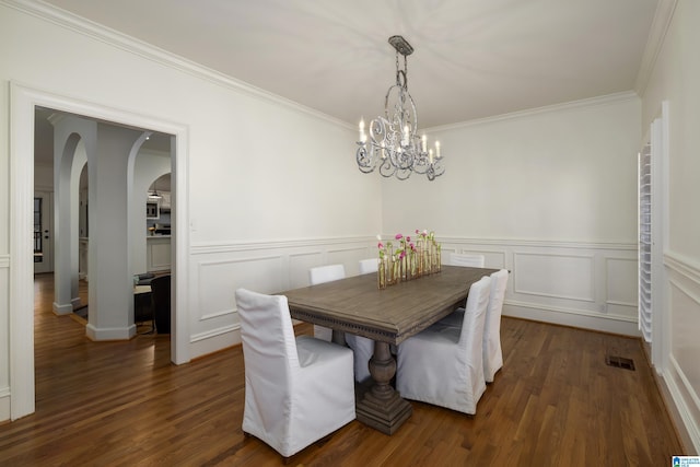 dining area featuring arched walkways, a wainscoted wall, visible vents, ornamental molding, and dark wood-style floors