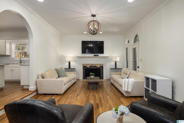 living room featuring arched walkways, a fireplace, light wood finished floors, an inviting chandelier, and ornamental molding