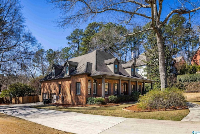 view of home's exterior featuring covered porch, brick siding, fence, driveway, and a lawn