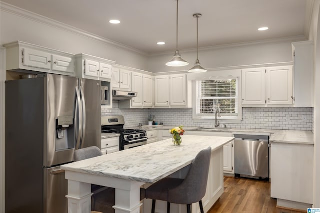 kitchen with white cabinets, a kitchen island, stainless steel appliances, under cabinet range hood, and a sink