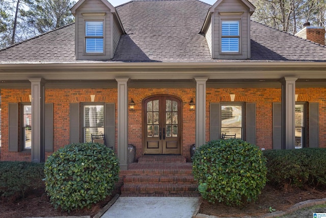 doorway to property with covered porch, roof with shingles, and brick siding