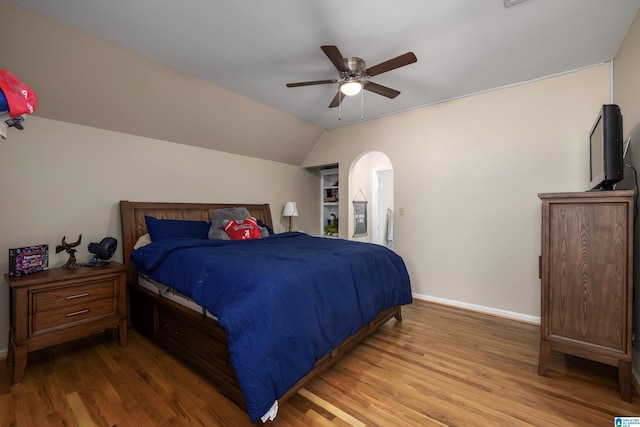 bedroom with arched walkways, baseboards, a ceiling fan, wood finished floors, and vaulted ceiling