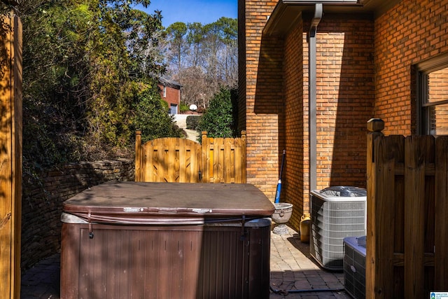 view of patio with a hot tub, a gate, fence, and central AC