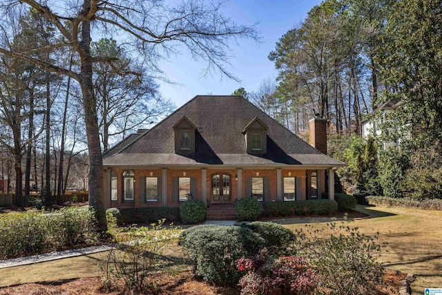 view of front facade with a porch, a front yard, brick siding, and a chimney