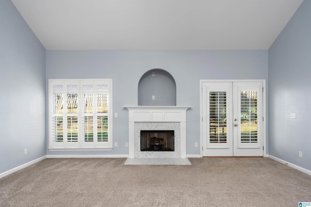 unfurnished living room with baseboards, french doors, a high end fireplace, and light colored carpet