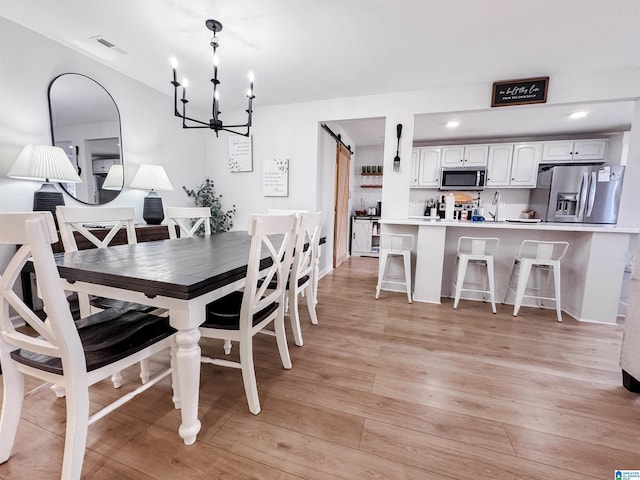 dining room featuring a barn door, light wood-style flooring, recessed lighting, a notable chandelier, and visible vents