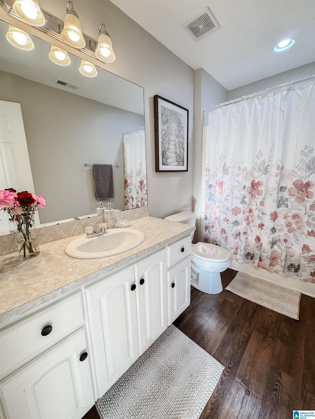 bathroom with toilet, wood finished floors, vanity, and visible vents