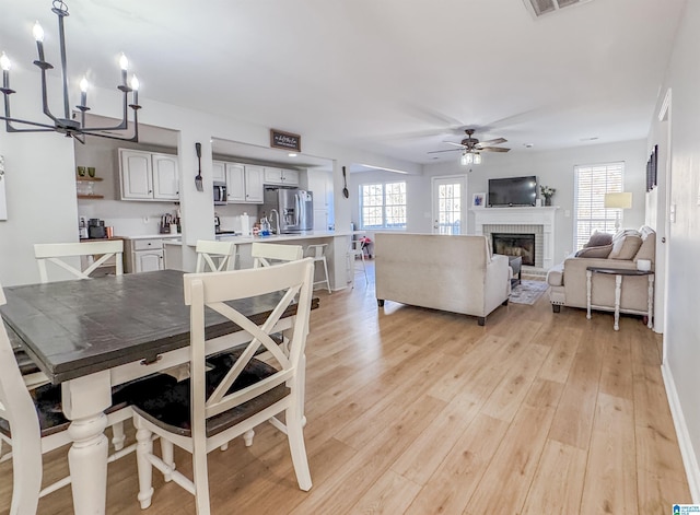 dining area with ceiling fan, a fireplace, visible vents, and light wood-style flooring