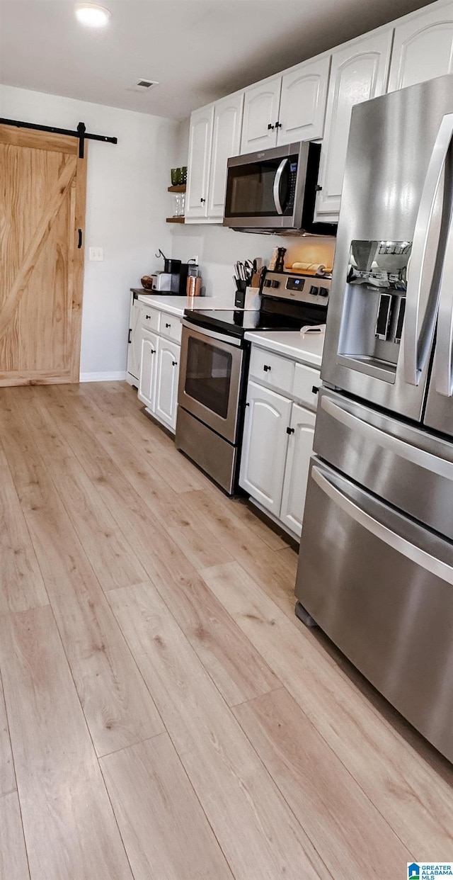 kitchen featuring stainless steel appliances, light countertops, a barn door, light wood-style floors, and white cabinets