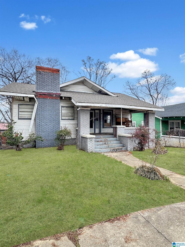 view of front facade with covered porch, roof with shingles, brick siding, and a front yard