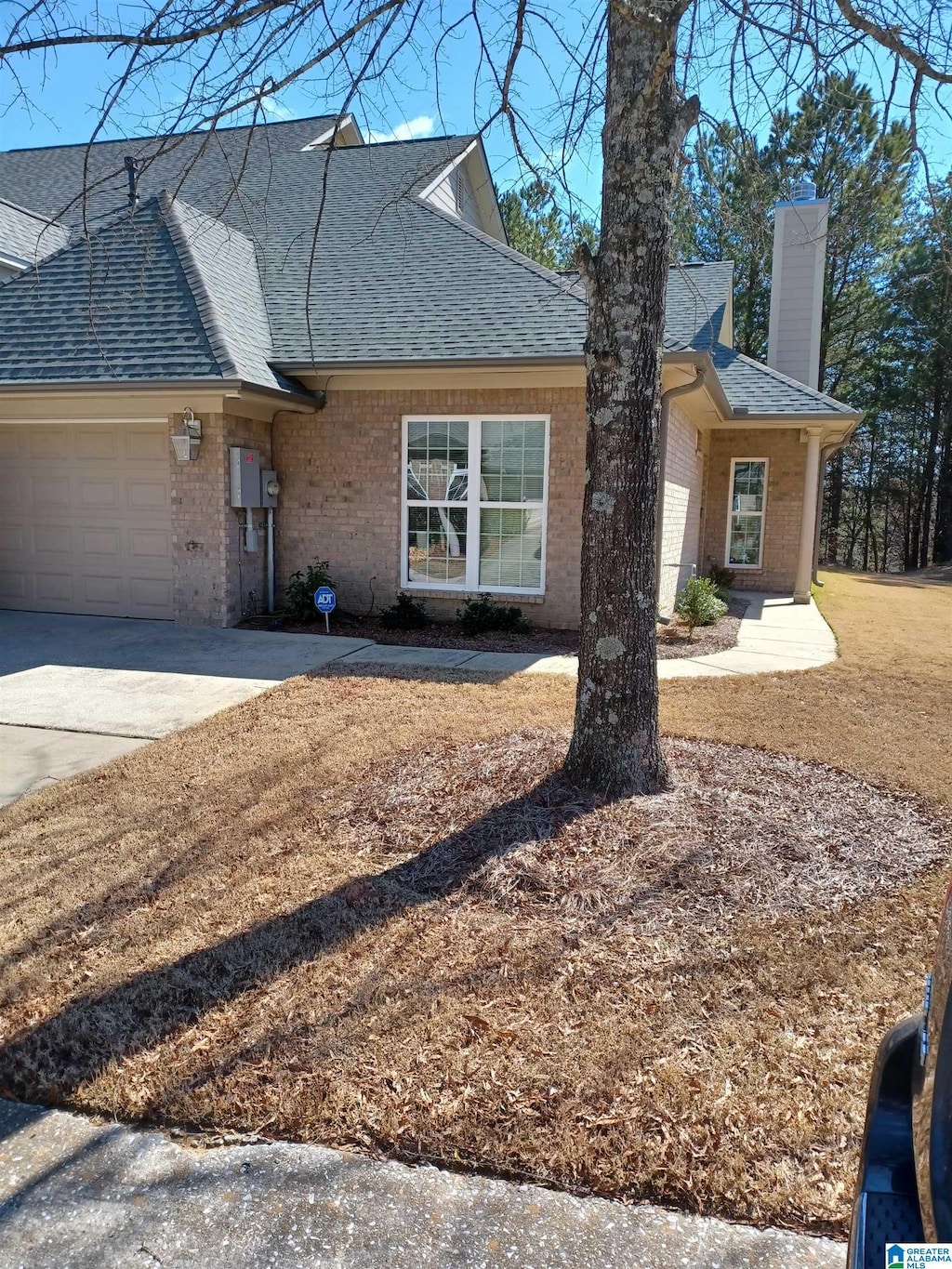 view of front of house with concrete driveway, a chimney, roof with shingles, an attached garage, and brick siding