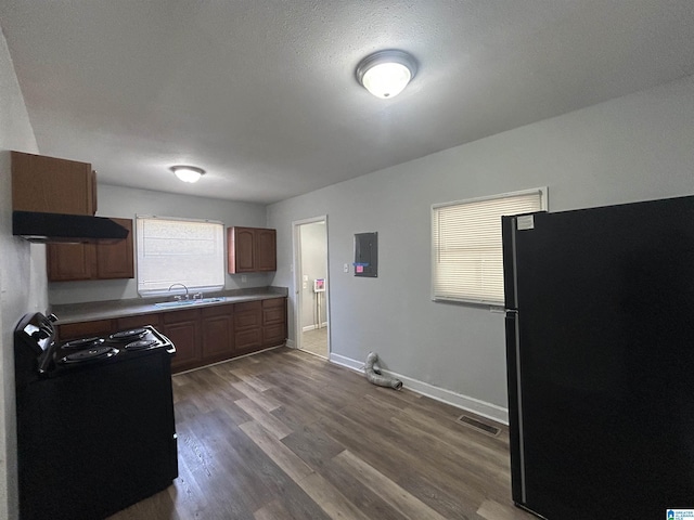 kitchen with light countertops, a sink, wood finished floors, under cabinet range hood, and black appliances