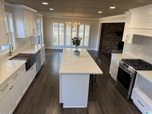 kitchen featuring a kitchen island, appliances with stainless steel finishes, hanging light fixtures, white cabinetry, and a sink