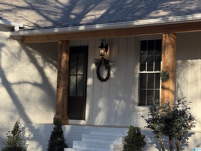 view of exterior entry featuring a shingled roof and brick siding