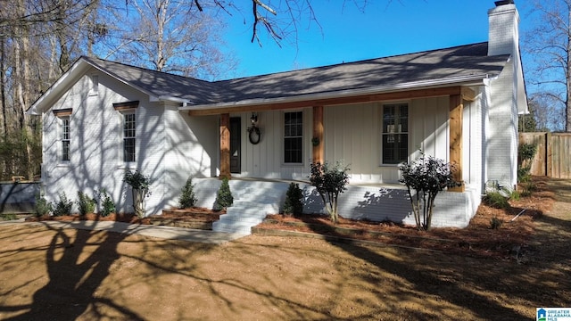 view of front of property featuring covered porch, a chimney, and brick siding