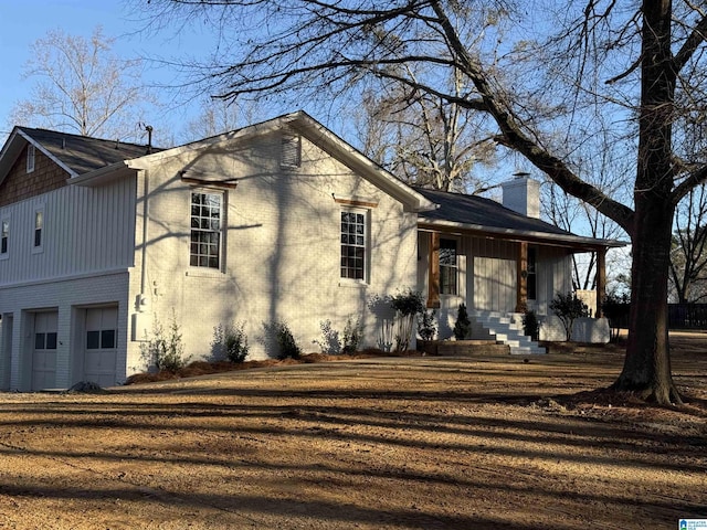 view of front of house with a porch, brick siding, a chimney, and a garage