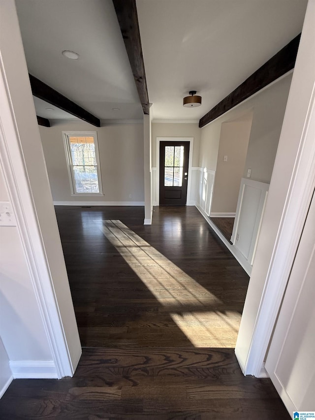 foyer entrance featuring a wainscoted wall, dark wood-style flooring, beam ceiling, and baseboards